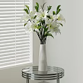 White Vase with White Lilies on Glass Round Table by White Blinds