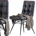 Black Leather Lounge Chair With Tufted Design And Gray Blanket On Metal Legs