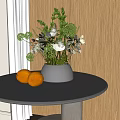 Silver Vase With White Flowers And Green Foliage On Round Marble Table With Oranges
