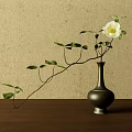 Black Ceramic Vase With White Flower And Green Leaves On Wooden Tabletop Against Beige Wall