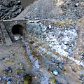 Stone Tunnel Entrance in Mountainous Terrain With Rocks Snow Patches and Slope Path