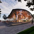 Modern Curved Glass Building Featuring Wooden Structure Trees Pathway People Walking And Bicyclist