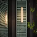 Warm Glow Modern Wall Sconce On Louvered Wall With Green Plants And Wooden Accents
