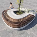 Curved Outdoor Chair Featuring Wooden Slats Concrete Base And Small Tree In Center
