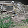 Outdoor Stone Structure With Wooden Beam Bench And Dirt Ground Surrounded By Grass