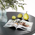 Glass Vase With Green Leafy Plants On Black Table With Yellow Pears And Open Magazine
