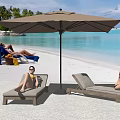 People Relaxing On Beach Lounge Chairs Under Umbrella With Palm Trees And Blue Ocean