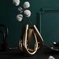 Golden Metallic Vase With Unique Loop Design Holding White Cotton Branches Against Dark Green Wall