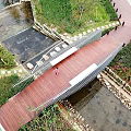 Wooden Landscape Bridge Spanning Stream With Green Vegetation And Paved Walkway