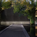 Dark Colored Building Facade With Golden Grille Windows Trees Water Pool Person And Reflection