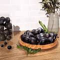 Black Fruits on Wooden Plate with Green Leaves Scattered Small Fruits Near Transparent Vase