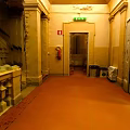 Cartoon Corridor Scene with Yellow Walls Red Carpet Columns and Green Exit Sign