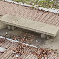 Outdoor Concrete Bench On Brick Pavement With Fallen Leaves And Snow Patches