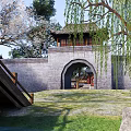 Ancient City Gate Architecture With Gray Brick Wall Wooden Bridge Weeping Willow And Green Grass