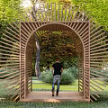 Wooden Pergola With Radial Slats Arched Entrance In Outdoor Garden Greenery People Walking