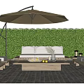 Outdoor Sofa With White Cushions And Wooden Coffee Table Under Patio Umbrella Against Green Hedge