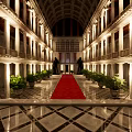 Grand Architectural Interior With Red Carpet Columns Symmetric Plants And High Ceiling