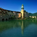 Scenic Garden Landscape With Serene Lake Clock Tower Mountain Backdrop And Lush Trees