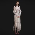 Woman in light colored long dress wearing glasses with hands crossed standing against black background