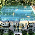 Roof Top Transparent Swimming Pool With People Swimming And Greenery Around Building