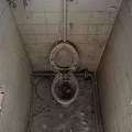 Dirty Old Toilet In Abandoned Bathroom With Cracked Tiles And Rusty Pipes