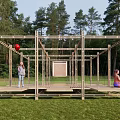 Wooden Frame Landscape Pavilion In Green Grassy Area With Surrounding Trees And People Relaxing