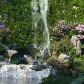 Park Landscape With Waterfall Lush Greenery Pink White Flowers Deer Family And Small Pond