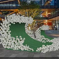 Outdoor Photo Spot With Green Wave Shaped Structure White Flowers And Modern Buildings