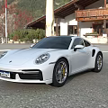 White Porsche Sports Car Parked Outdoor With Building And Mountain View