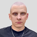 A Bald Head Man in Black Turtleneck Sweater with Silver Necklace Against Light Gray Background