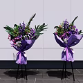 Elegant Floral Display With Purple Wrapped Bouquets On Black Tripods Against White Wall