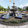 Elegant Central Fountain With Surrounding Colorful Flower Beds And Modern Glass Building Background