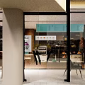Modern Dessert Shop Exterior With Glass Facade Signboard Warm Lighting And Interior Seating