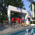 Outdoor Scene With White Archway Red Car Woman Green Plants Tables Chairs Bicycle And Pool