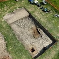 Top Down Aerial View Of Outdoor Archaeological Excavation Trench On Grassy Site With Working Tools