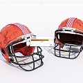 Two Orange Football Helmets With Red White Stripes And Black Facemasks