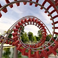 Thrilling Red Spiral Roller Coaster Track Among Green Trees Water And Blue Sky