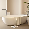 White Freestanding Bathtub in Beige Bathroom with Towel Slippers and Bamboo Plant