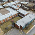 Aerial View Of Multiple Brick And Metal Buildings With Gray Roofs And Parking Lot