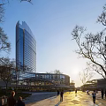 Vibrant Modern Commercial Street with Tall Glass Building Deciduous Trees Sunlight and Pedestrians Walking