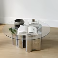Round Glass Coffee Table with Silver Metal Base Open Book Decorative Bowl and Small Plant