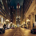 Illuminated Nighttime Commercial Street With Tall Buildings Street Lamps And Parked Cars