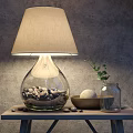 Table Lamp with Glass Base Fabric Shade Pebbles on Wooden Table and Green Plant