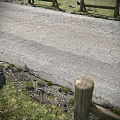 Road Infrastructure Cracked Asphalt Pavement With Grass Verge And Wooden Fence