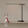 White Rabbit Figurine With Red Scarf And Black Modern Desk Lamp On Light Colored Shelf