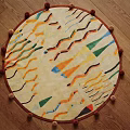 Round Rug With Colorful Geometric Patterns And Pom Pom Trim On Wooden Floor
