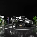 Black MPV Car Showcase On Circular Platform With Green Plants And Screens