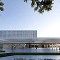 Modern Building With Glass Curtain Wall In Open Plaza With Pedestrians And Trees