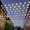 Round Shaped Decorative Lights Hanging Above Outdoor Space With Buildings And Green Plants