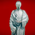 Mysterious Game Movie Character With White Mask Gold Spiral Eyes And Mesh Clothing On Red Background